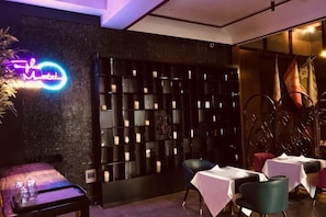 A restaurant with a neon sign, a black wall with shelves, and tables with white tablecloths. - Bremen Hotel (Harbin)