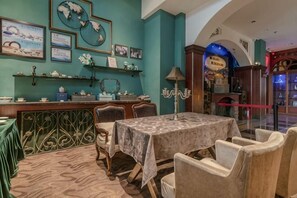 A dining area with a table set for four, chairs, a chandelier, and wall-mounted shelves with decorative items. - Bremen Hotel (Harbin)