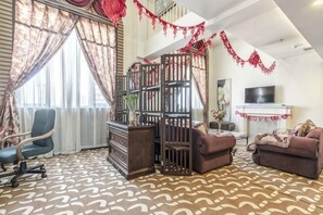 A living room with a patterned carpet, a sofa, a chair, a TV, and a decorative gate. - Bremen Hotel (Harbin)