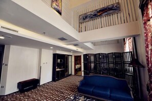 A hotel lobby with a blue sofa, a patterned carpet, and a high ceiling with a decorative panel.