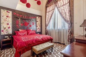 A bedroom with a large bed, a bench, a bedside table, and a headboard with decorative elements. - Bremen Hotel (Harbin)