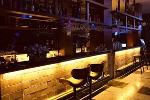 A bar area with a brick counter, shelves with bottles, and two chairs.