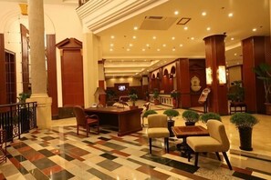 A lobby with a check-in counter, seating area, and a staircase leading to upper floors.
