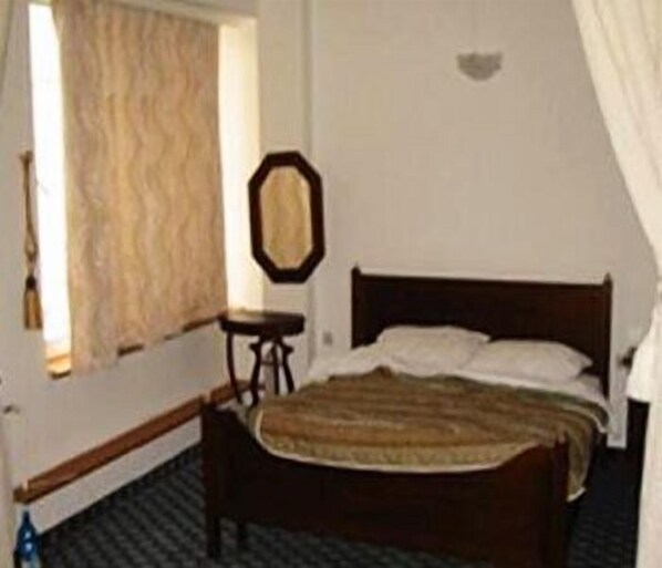 A bedroom with a wooden bed, a small table, and a window with curtains.