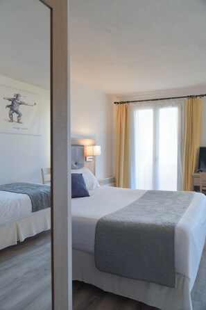A hotel room with two beds, a large window with curtains, a bedside lamp, and a wall-mounted artwork.