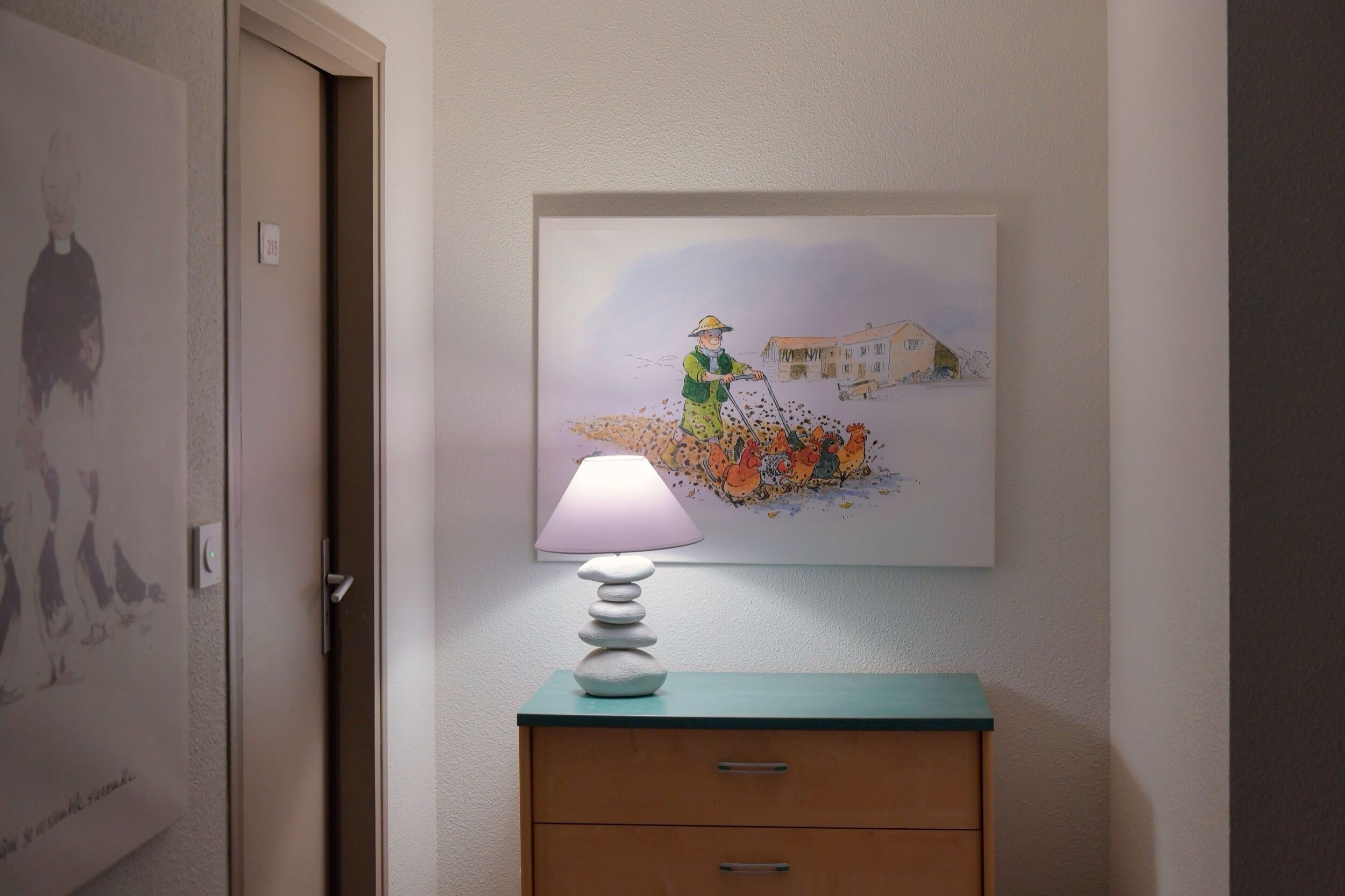 Un pasillo con una puerta, una lámpara de pared, una obra de arte enmarcada y un armario de madera.