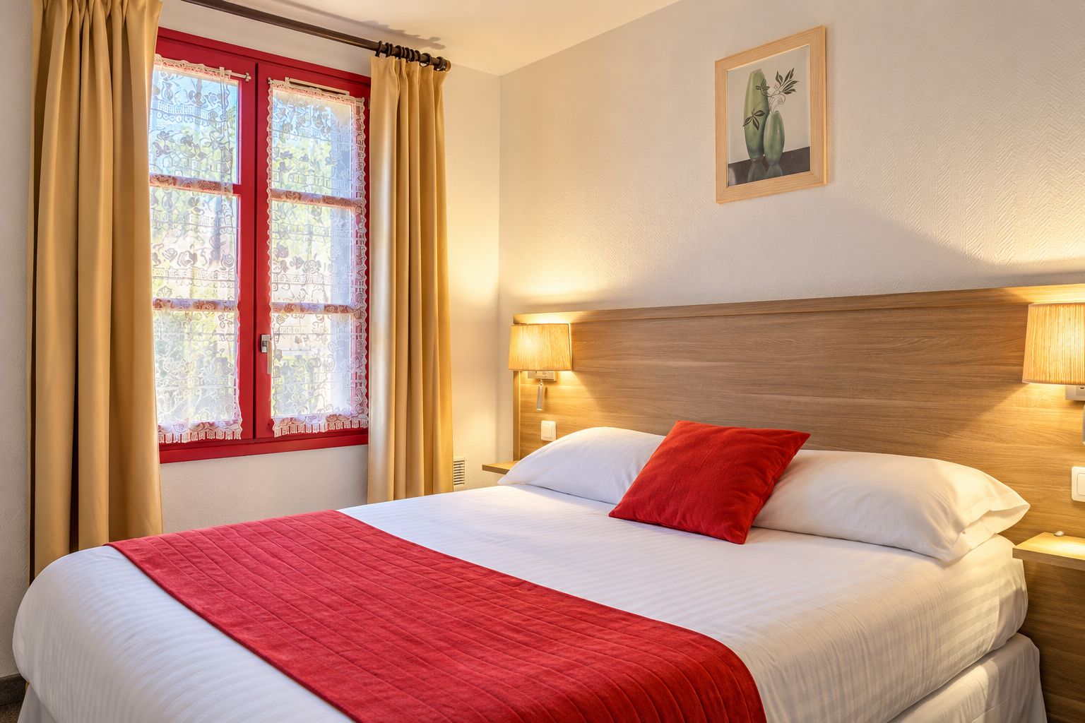 A hotel room with a bed, a window with curtains, a wall-mounted lamp, and a framed picture.