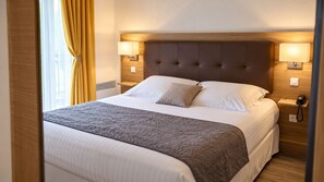 A hotel room with a large bed, two bedside lamps, a telephone, and a window with curtains. - Logis Hôtel Les Comtes De Pardiac (Marciac)
