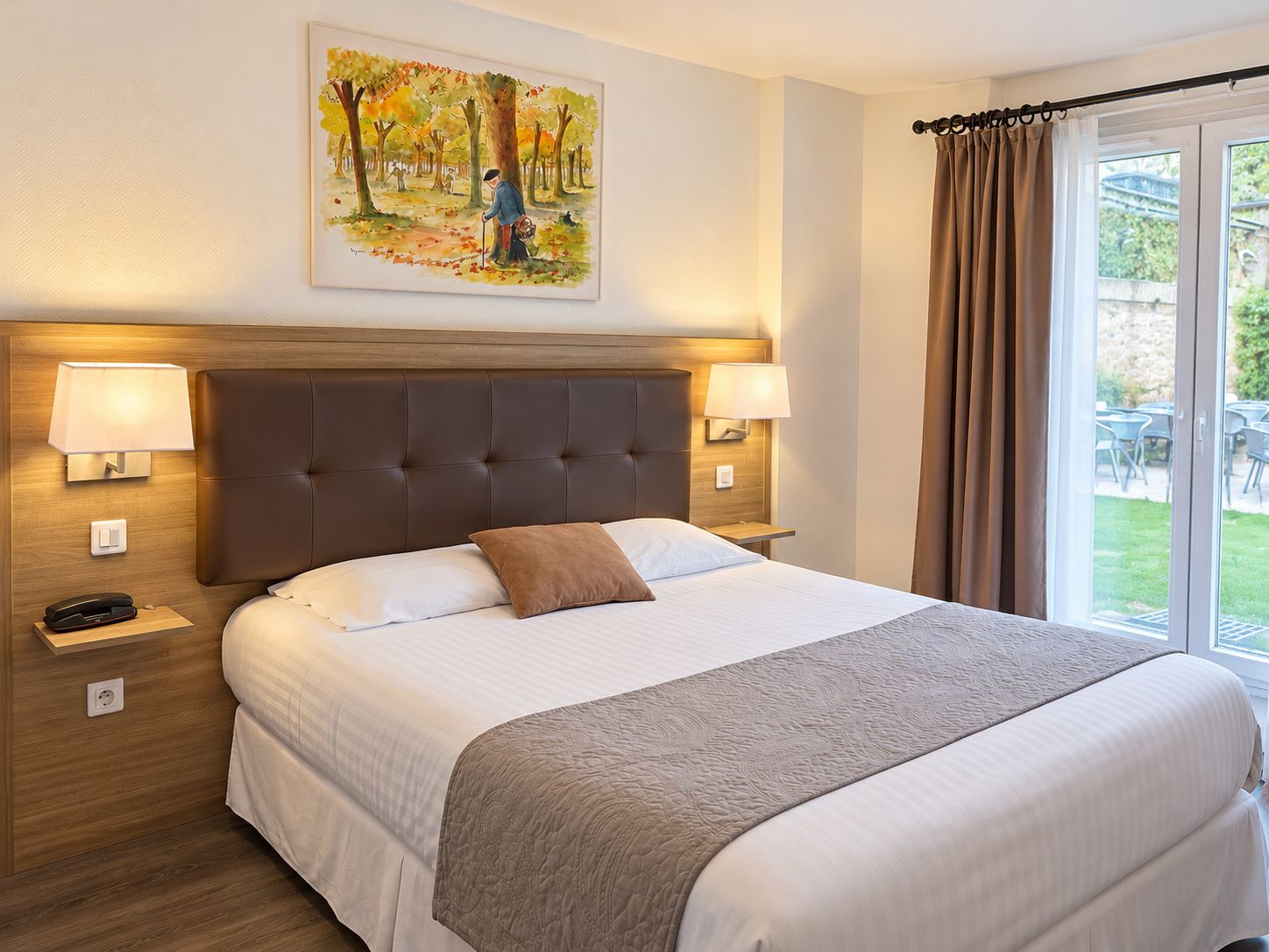 A hotel room with a large bed, two bedside lamps, a painting of a forest scene, and a view of the outdoors through a window with curtains.