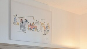 Habitación de hotel con cama, cabecero, lámpara de noche y una obra de arte colgada en la pared.