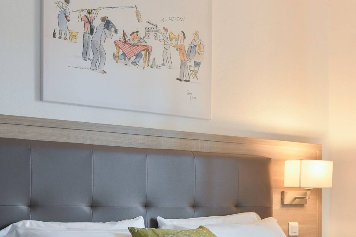 Ein Hotelzimmer mit einem Bett, einem Kopfteil, einer Nachttischlampe und einem an der Wand hängenden Kunstwerk.