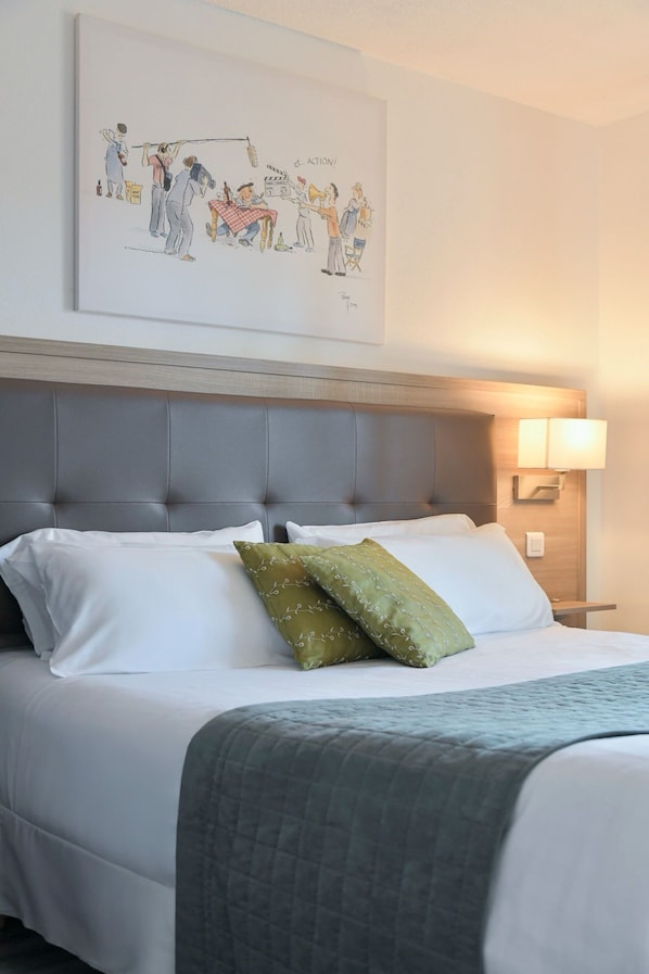 Habitación de hotel con cama, cabecero, lámpara de noche y una obra de arte colgada en la pared.