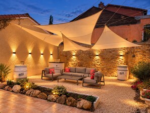 An outdoor seating area with a sofa and chairs, surrounded by a stone wall and a large shade sail. - Logis Hôtel Les Comtes De Pardiac (Marciac)