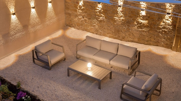 Un espace extérieur aménagé avec un mur en pierre, un canapé, deux fauteuils et une table basse.