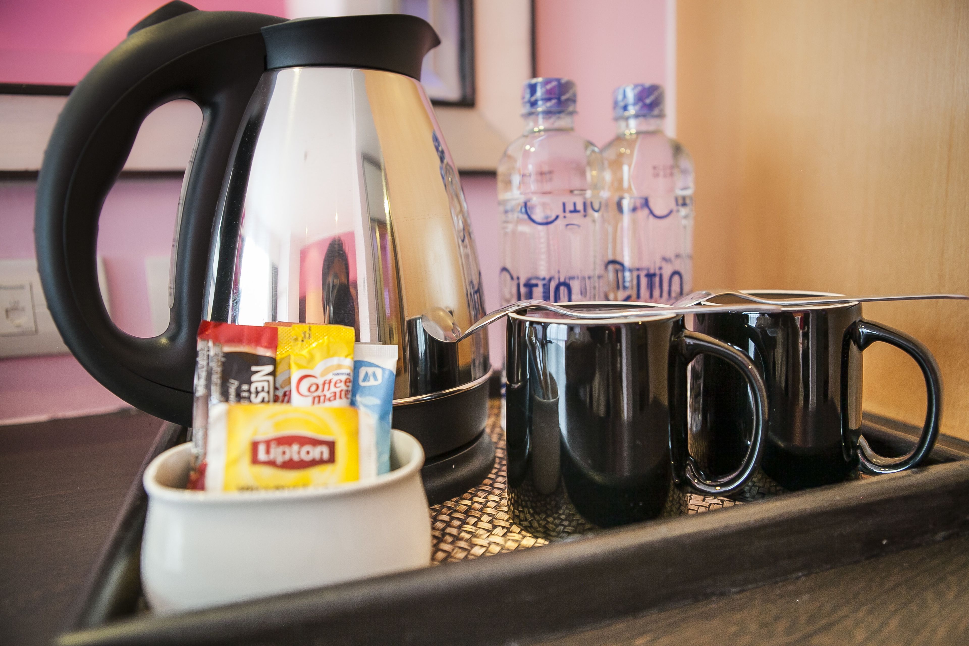 Un taulell de cuina amb una cafetera, dues tasses negres, una tassa blanca amb sobres de cafè i dues amples de l'aigua.