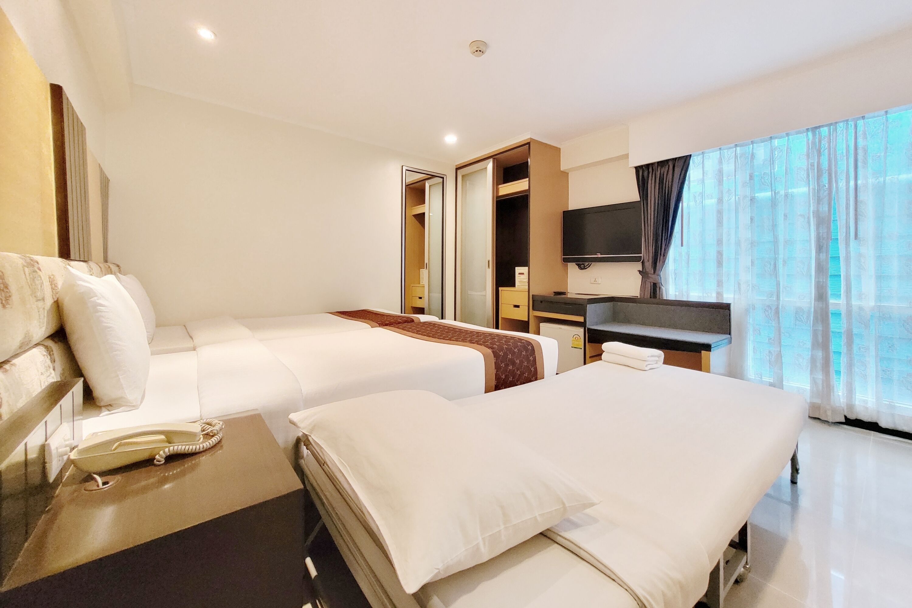 Habitación de hotel con dos camas, un escritorio, un televisor y un ventanal con cortinas.