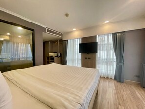Habitación de hotel con una cama grande, un televisor de pantalla plana montado en la pared, un escritorio con computadora y una ventana con cortinas.