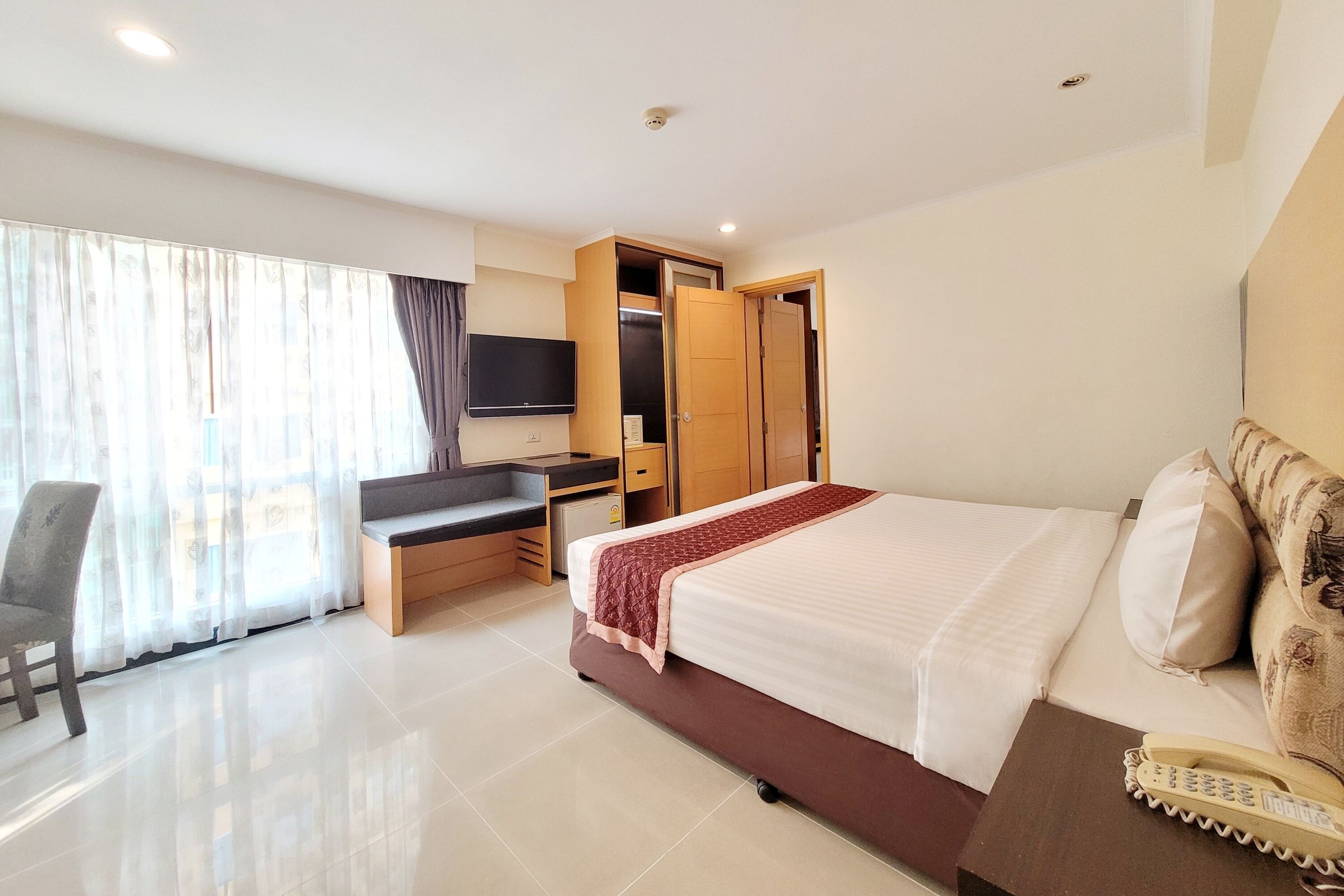 A hotel room with a bed, a desk, a chair, a TV, and a wardrobe.