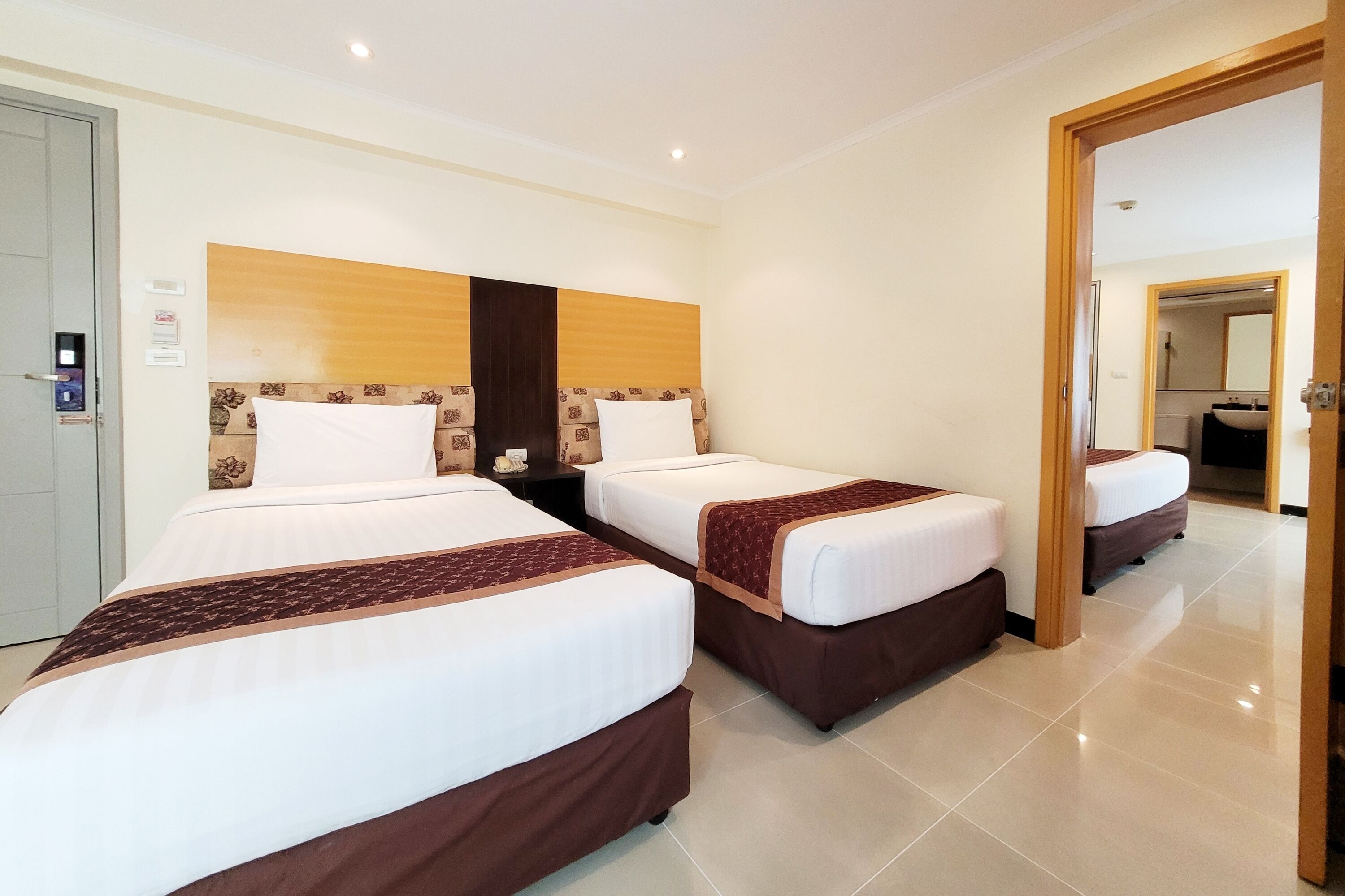 A hotel room with three beds, a wooden headboard, and a mirror.