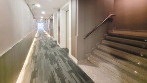 A hotel hallway with a carpeted floor, a staircase, and a door at the end. - Citin Pratunam Bangkok Hotel by Compass Hospitality (Bangkok)