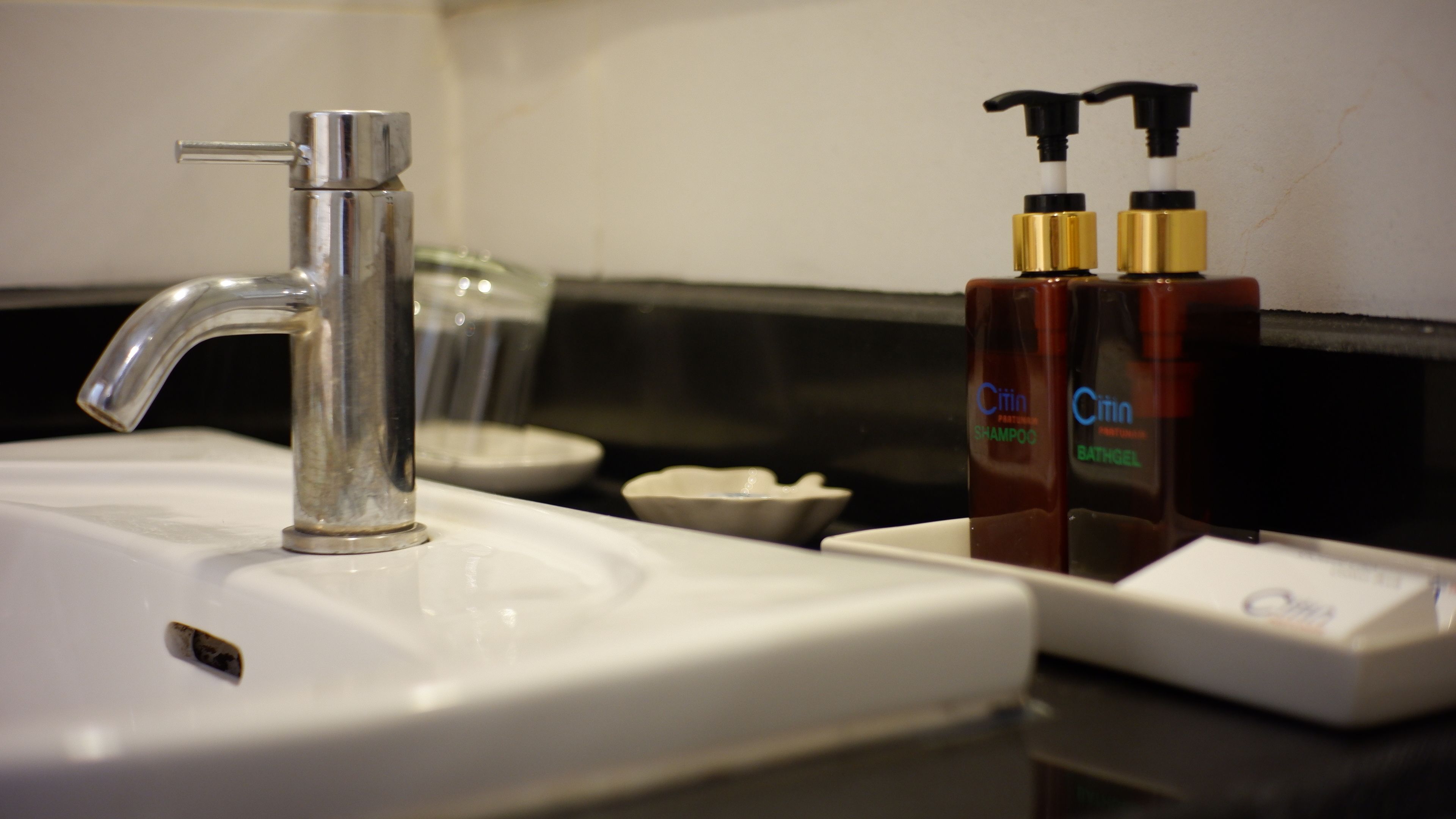 Un lavabo de salle de bain avec un robinet moderne, deux bouteilles de shampoing et de gel douche au citron, et un porte-savon.