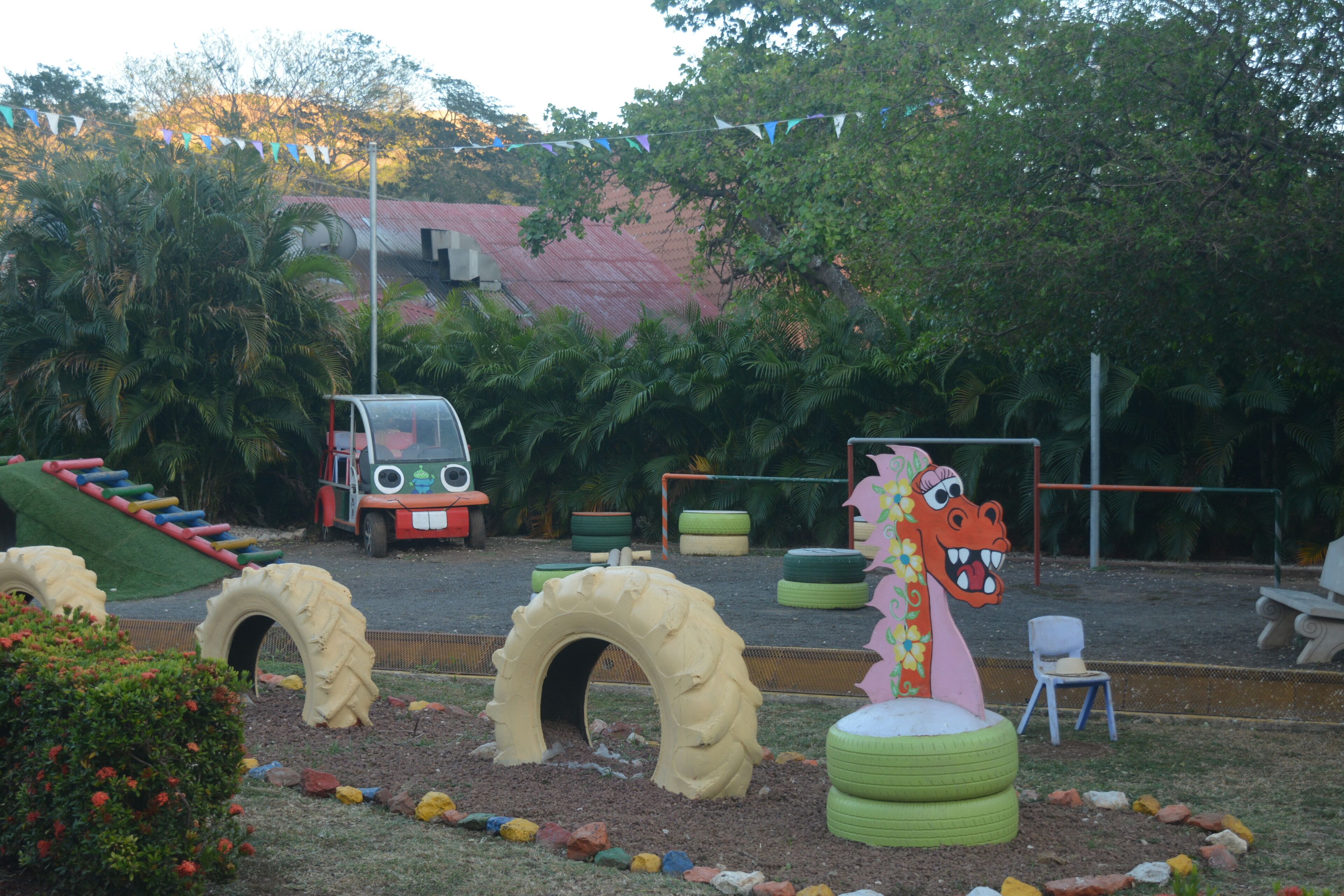 A playground with tire arches, a slide, and a play structure resembling a dinosaur.