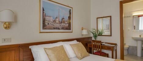 A hotel room with a bed, a desk with a chair, a telephone, a lamp, a framed picture on the wall, and a mirror.