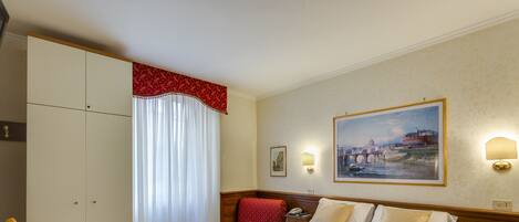 A hotel room with a bed, a desk with a chair, a nightstand, a lamp, and a painting on the wall.