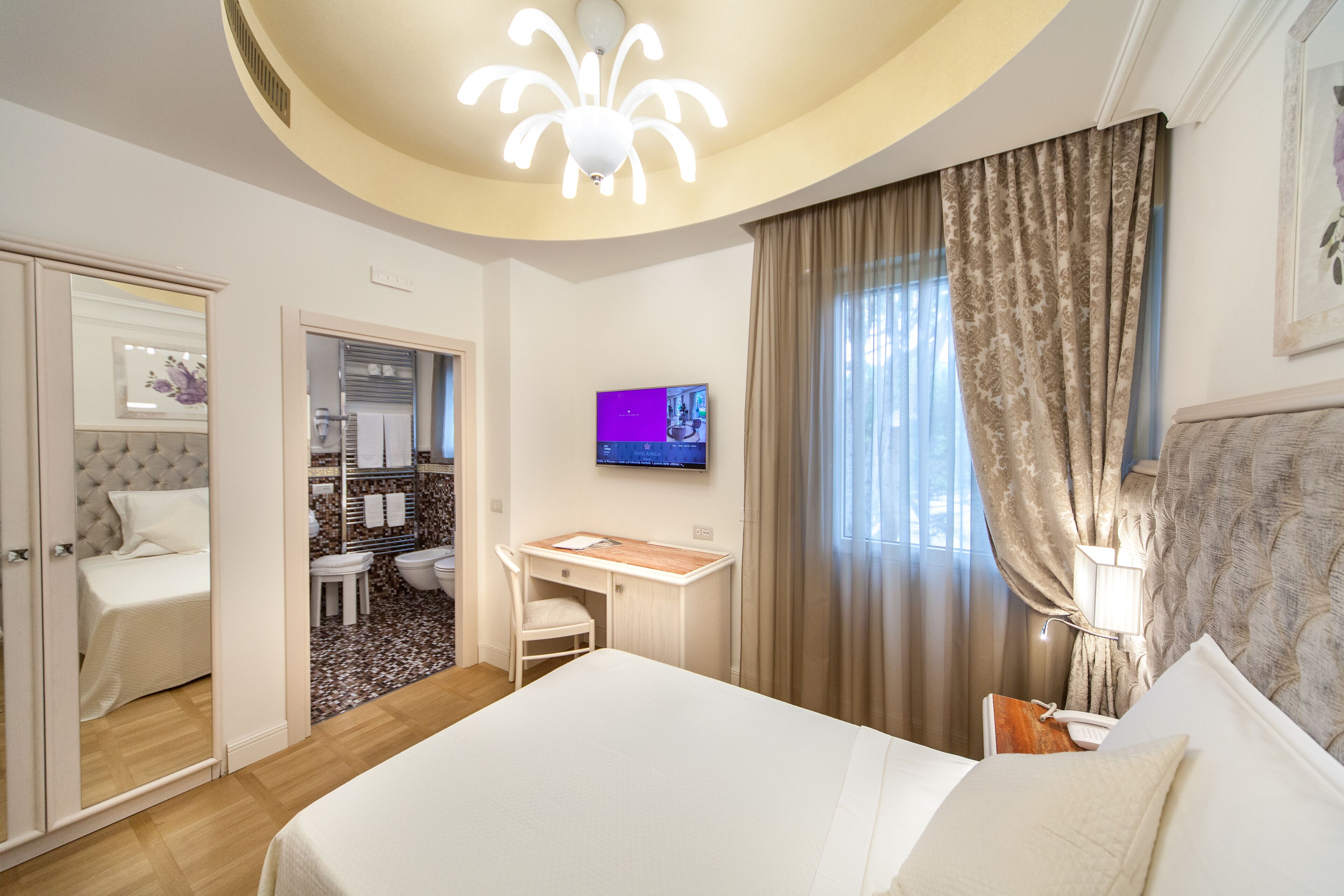 A hotel room with a bed, a desk, a TV, and a bathroom.