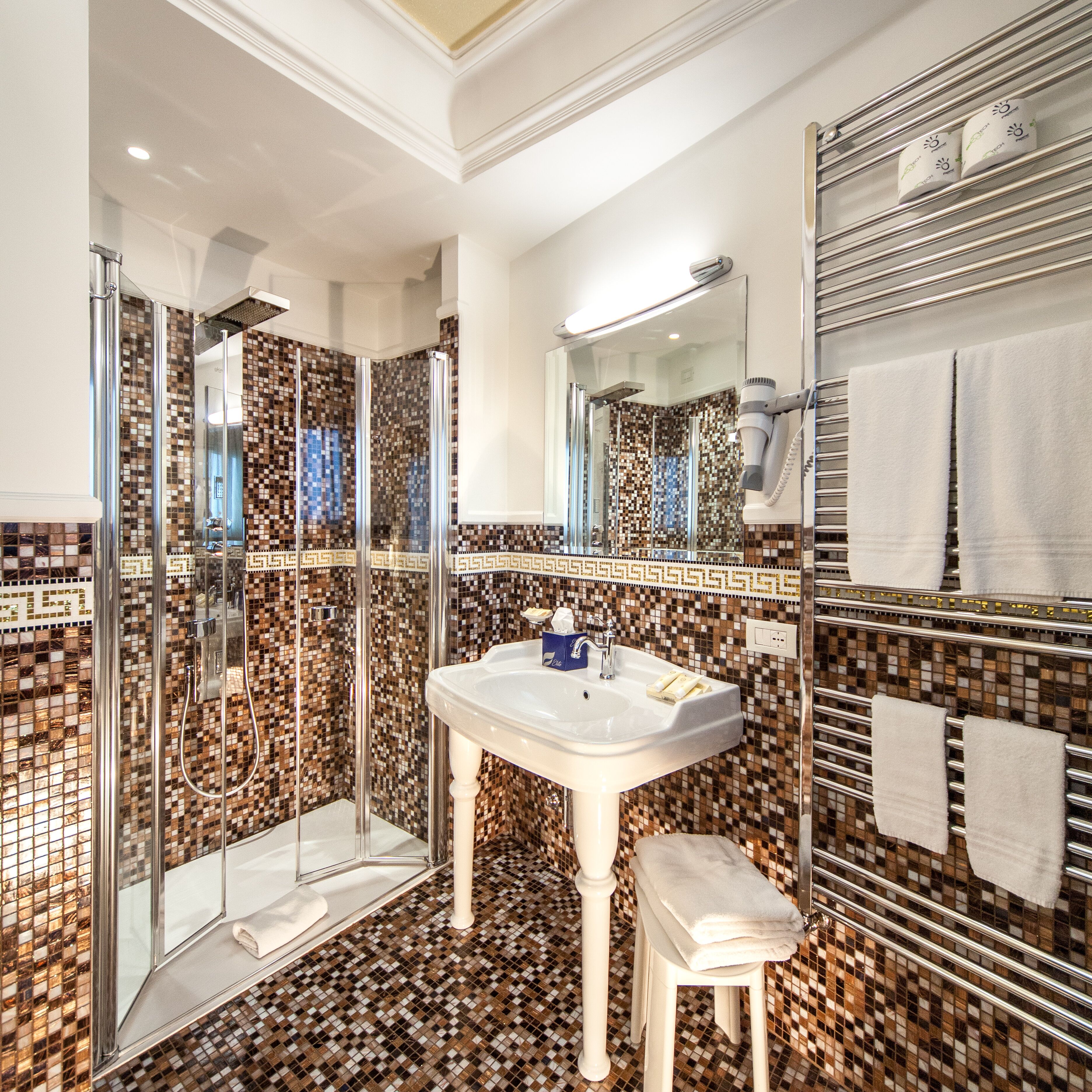 Une salle de bain dotée d’une douche à parois de verre, d’un lavabo sur pied blanc et d’un sol carrelé.