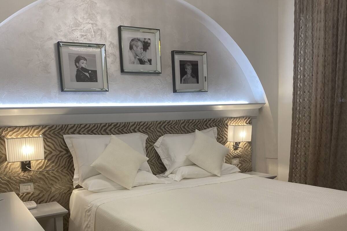 A neatly arranged bedroom with a large bed, a bedside table, a lamp, and framed pictures on the wall.