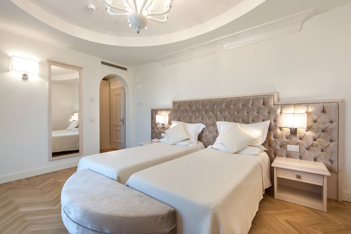A hotel room with two beds, a large mirror, a chandelier, and a wooden floor.