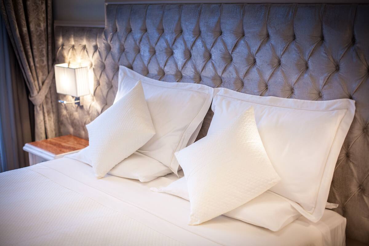 A neatly made bed with white linens and pillows, a tufted headboard, and a bedside lamp.