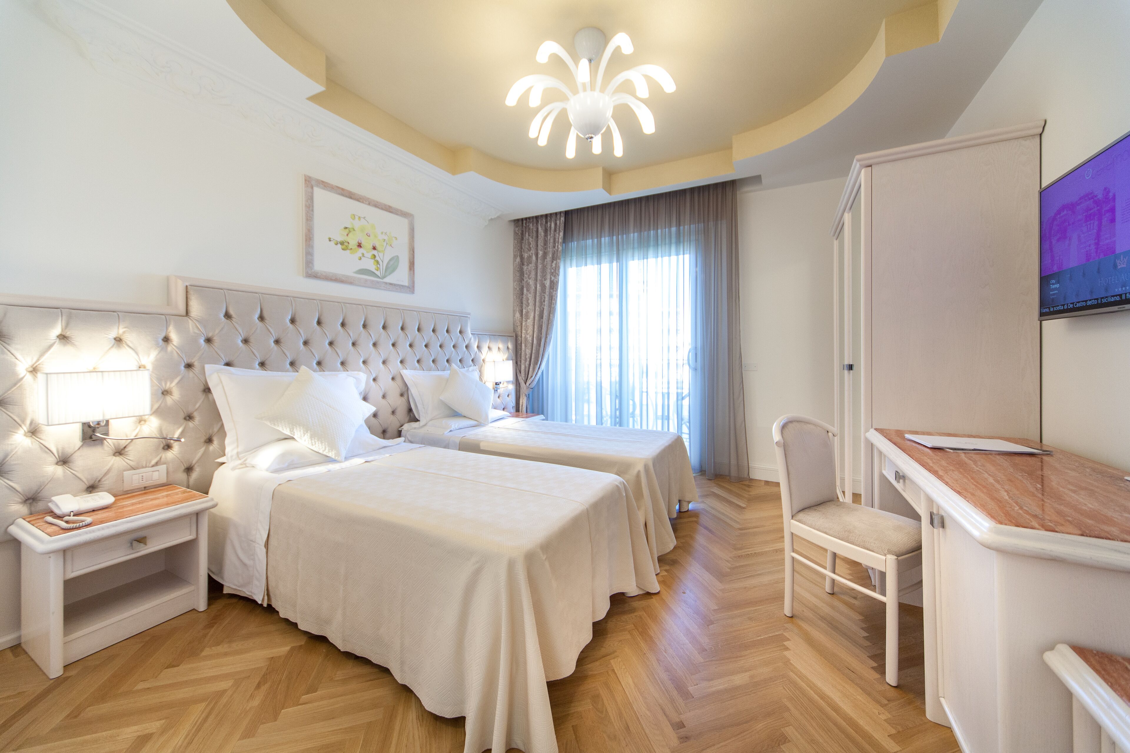 A hotel room with two beds, a desk, a chair, a TV, and a ceiling light.