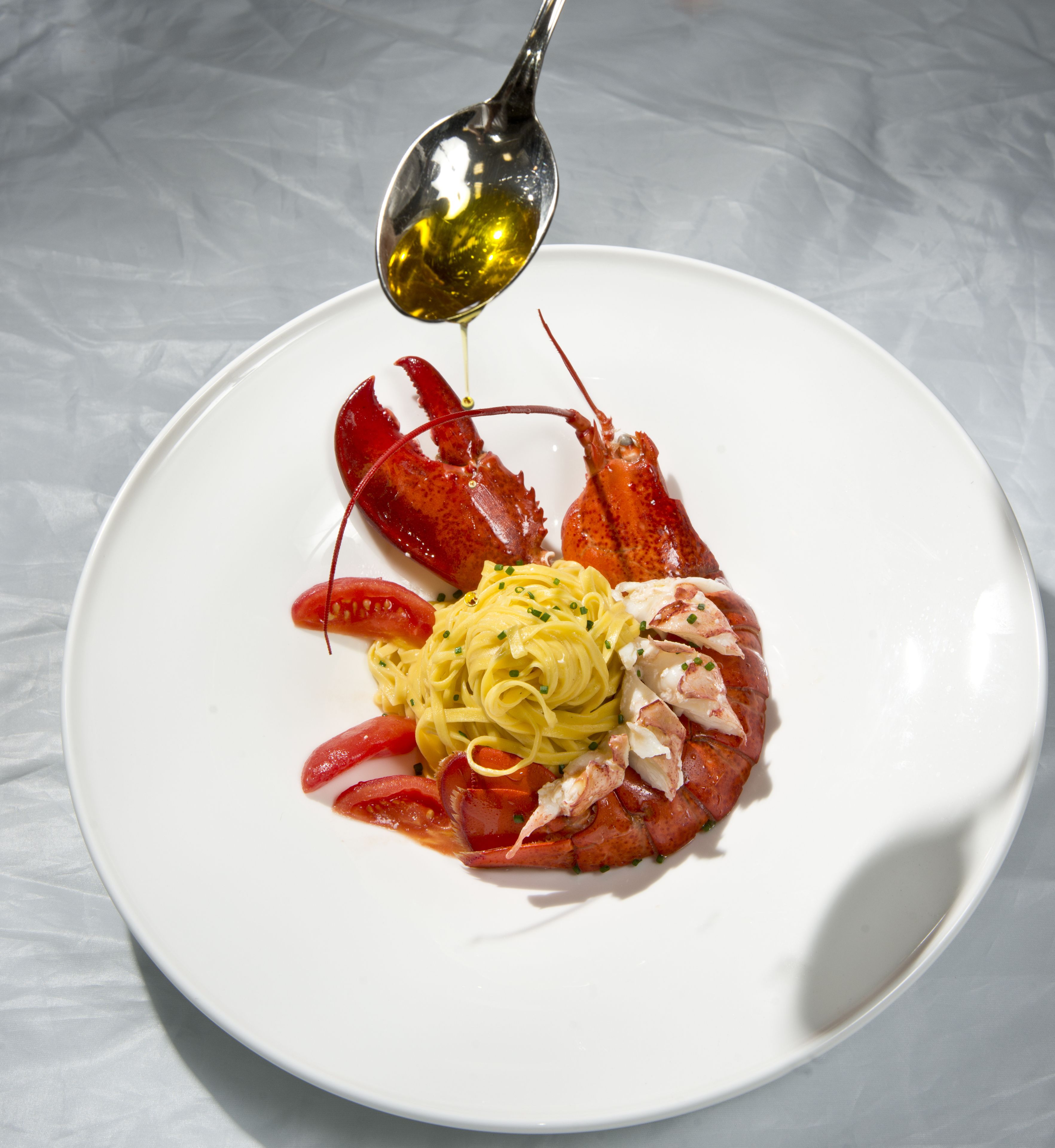 A plate with pasta, lobster, and a spoonful of sauce.