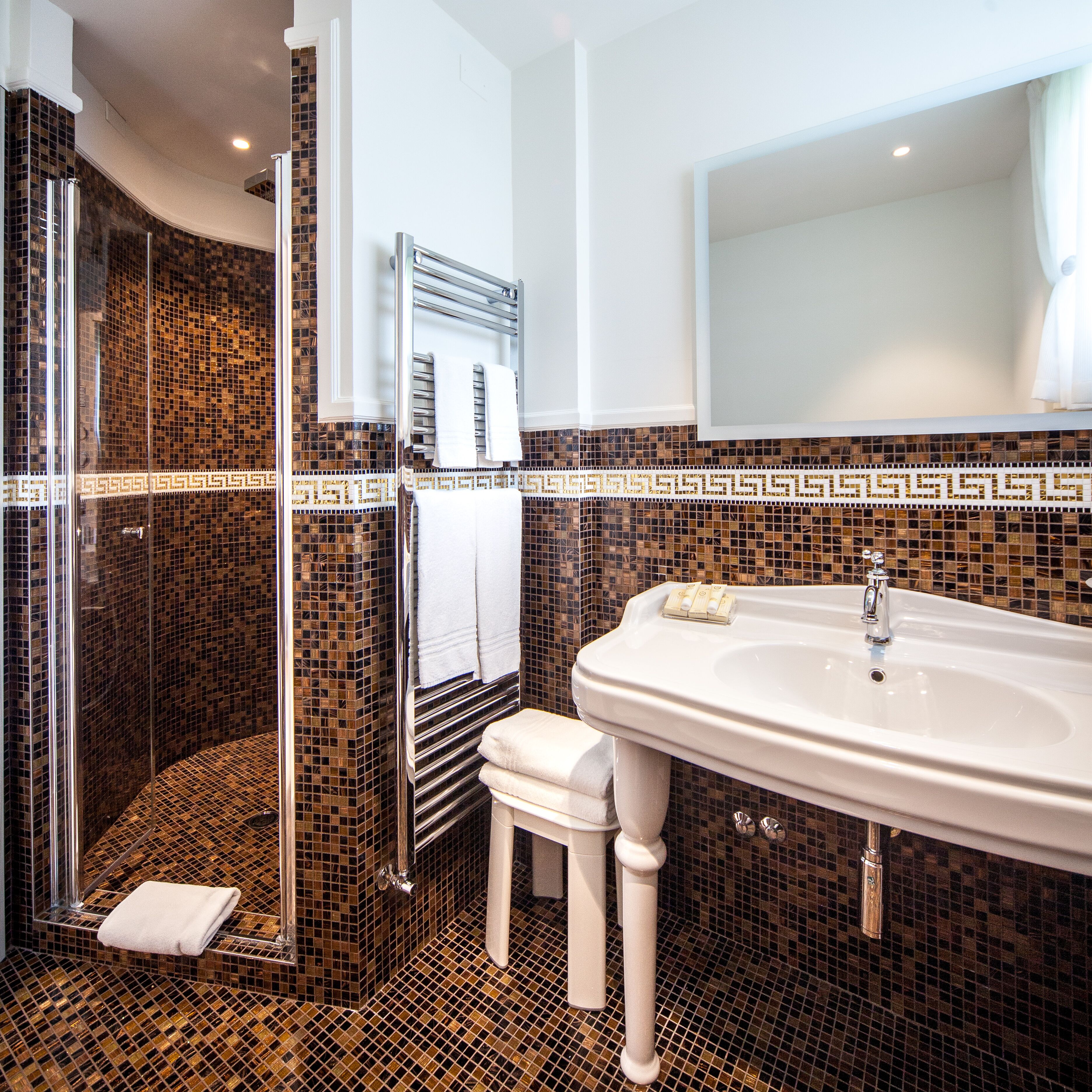 A bathroom with a large sink, a glass shower enclosure, and a small stool.