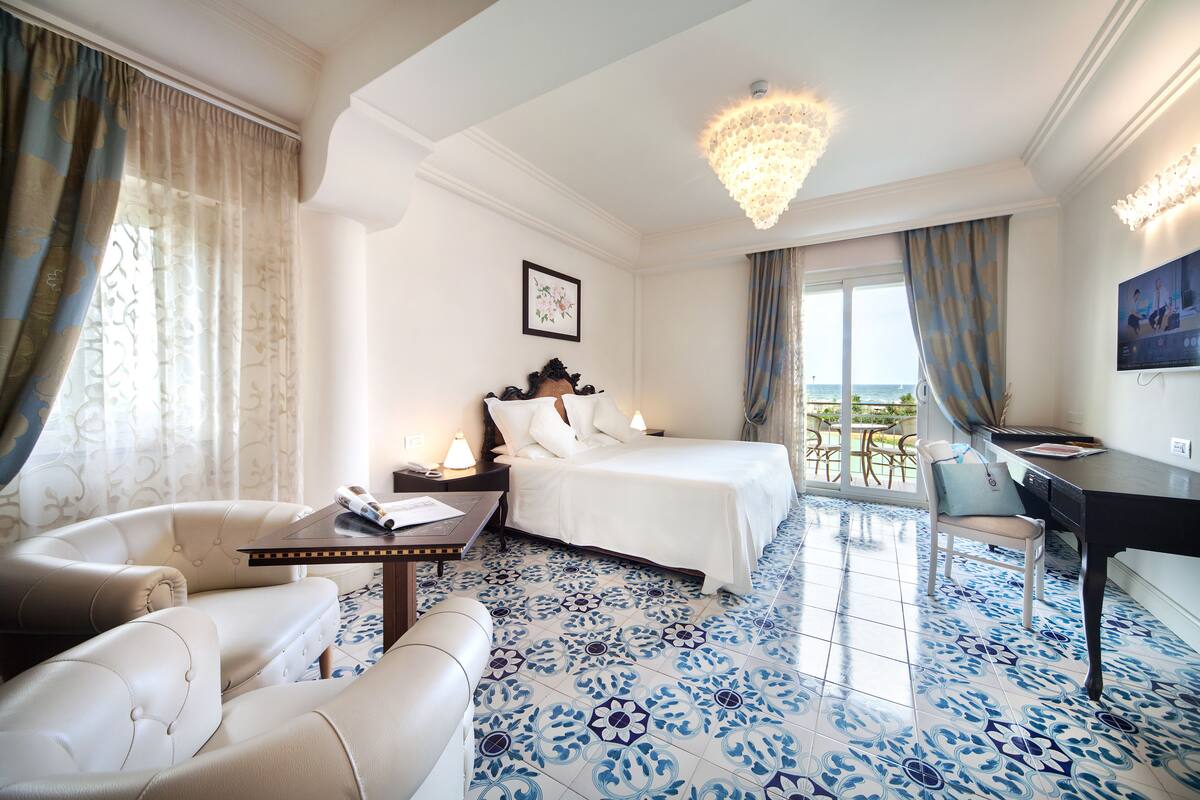A hotel room with a bed, a desk, a chair, and a balcony with a view.