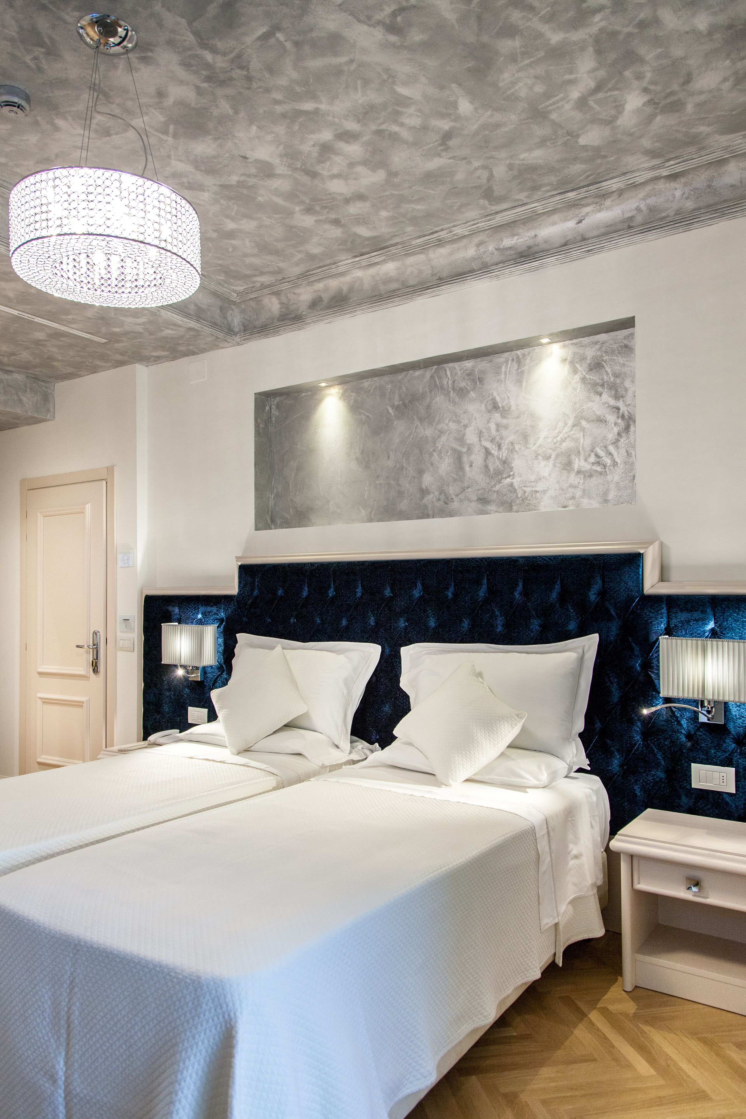 A large bed with white linens, a dark blue headboard, and two bedside lamps.
