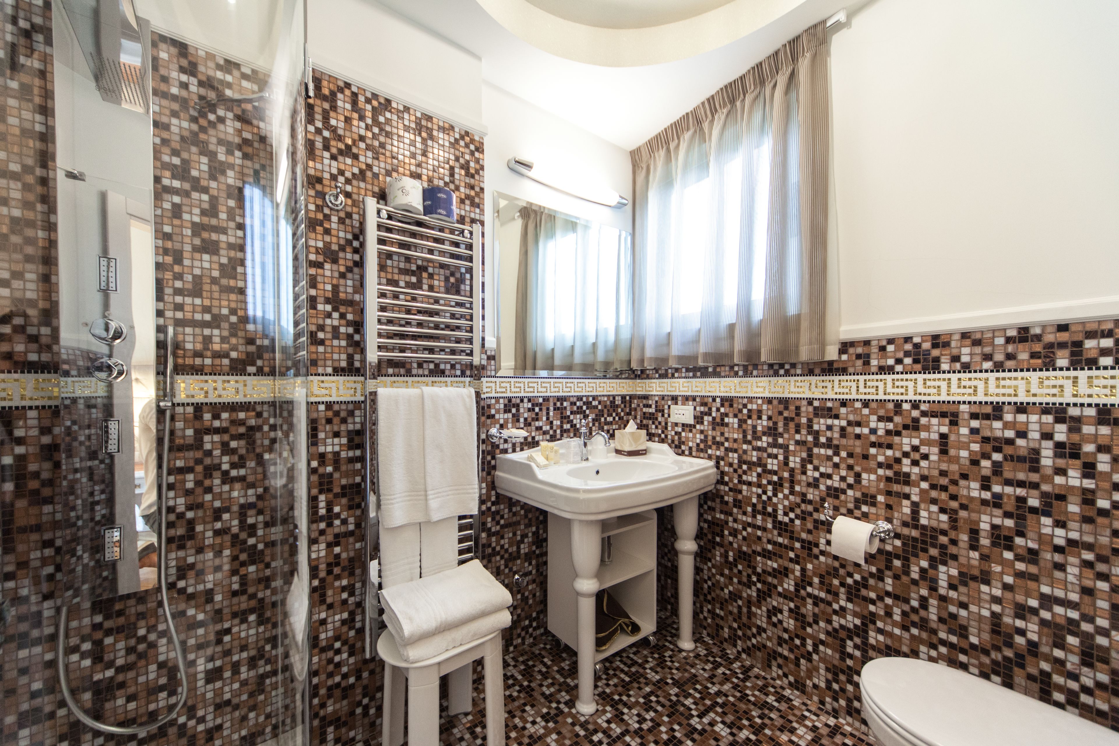 A bathroom with a tiled mosaic backsplash, a white sink, a glass shower enclosure, and a toilet.