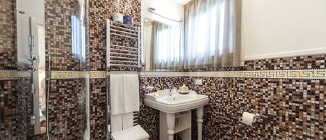 A bathroom with a tiled mosaic backsplash, a white sink, a glass shower enclosure, and a toilet.