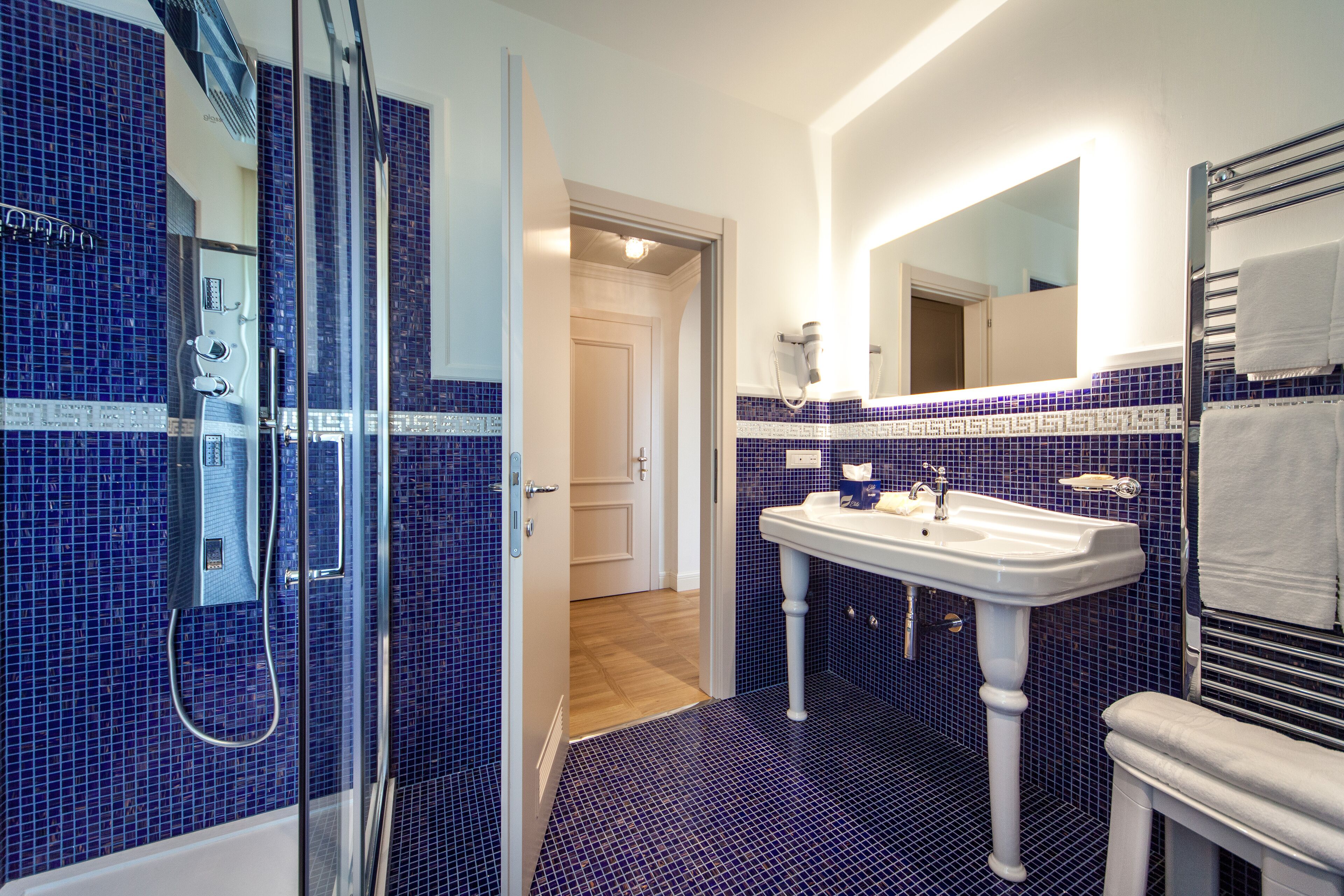 Un baño con cabina de ducha de vidrio, un lavabo pedestal blanco y un espejo sobre el lavabo.