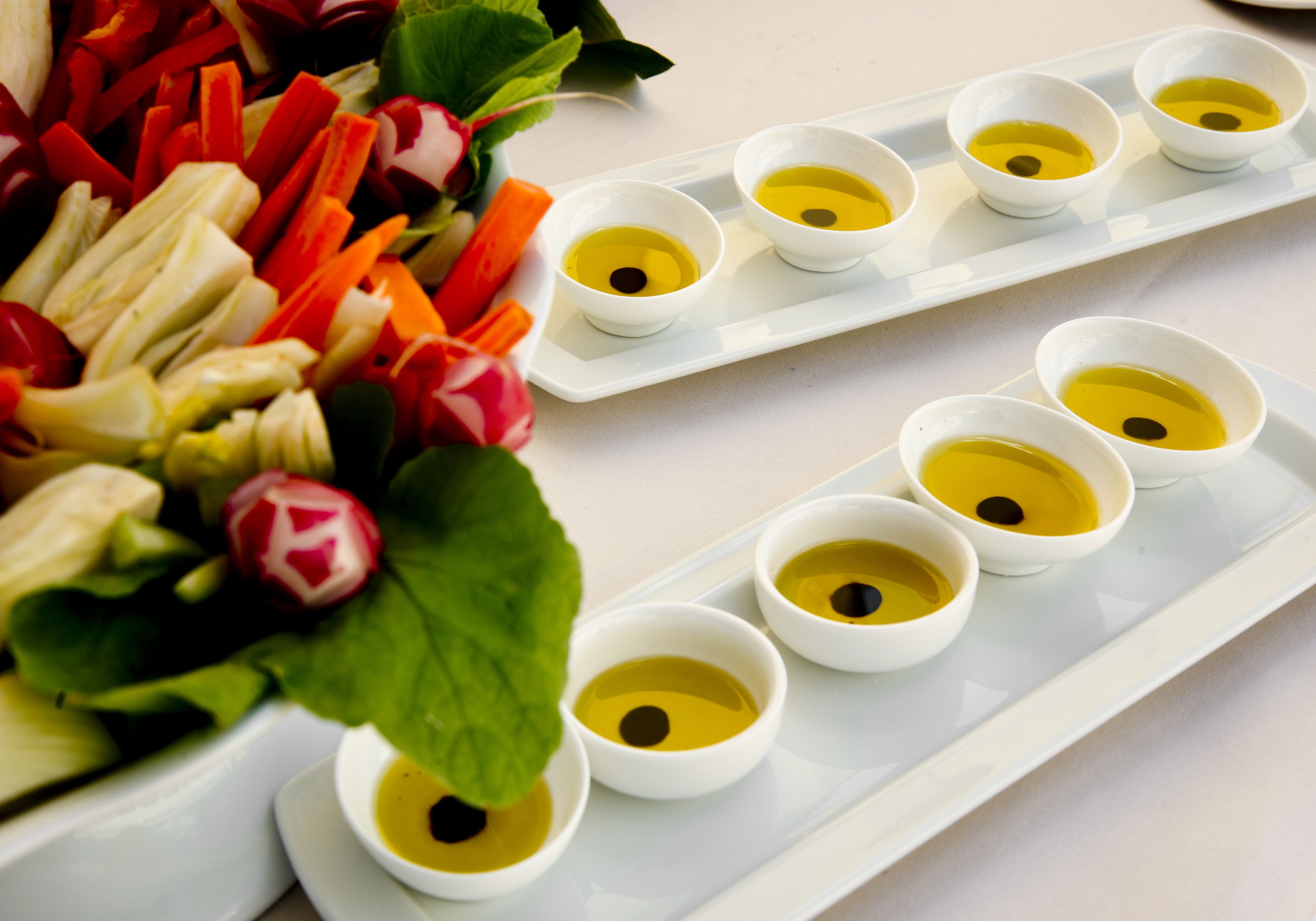 A white tray with small bowls of yellow liquid and a variety of sliced vegetables.