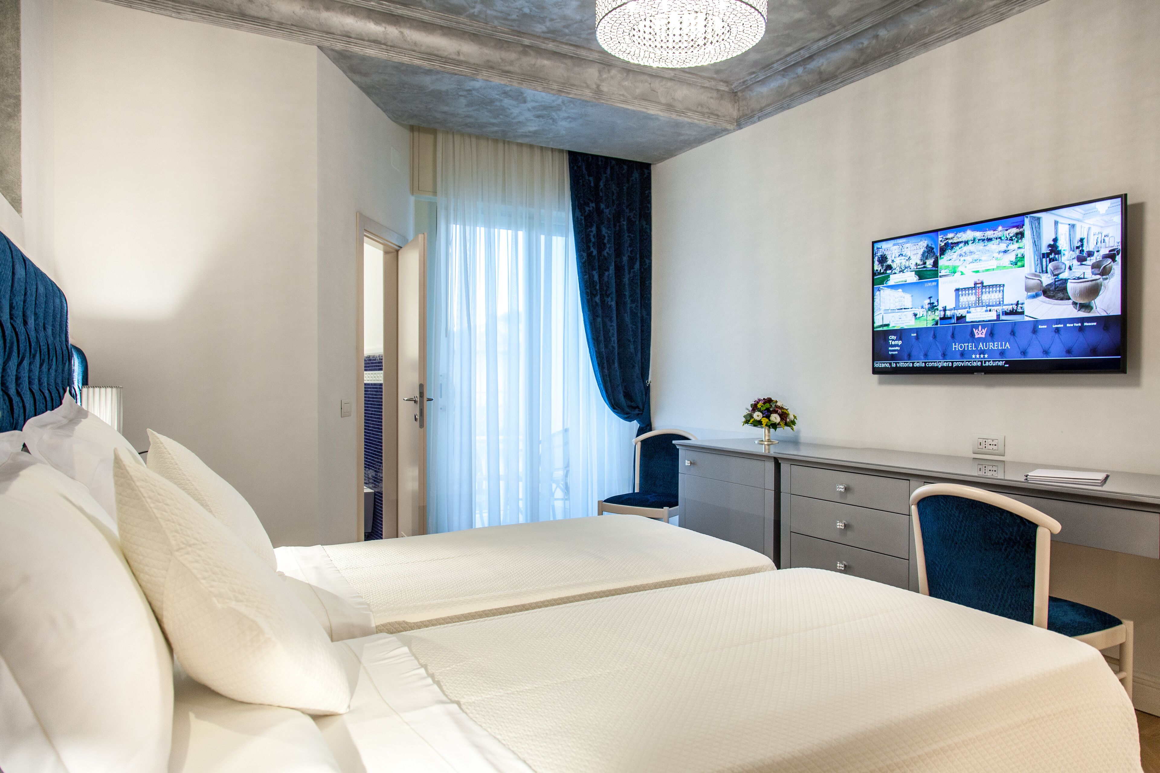 A hotel room with two beds, a desk, and a television displaying the hotel's website.