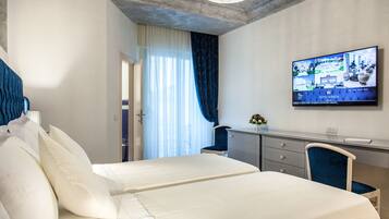 A hotel room with two beds, a desk, and a television displaying the hotel's website.