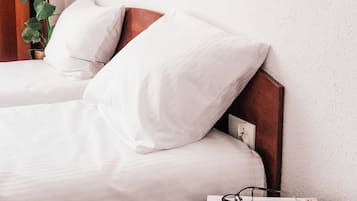 Habitación de hotel con dos camas, una lámpara de pared, una planta y una revista sobre una mesita.