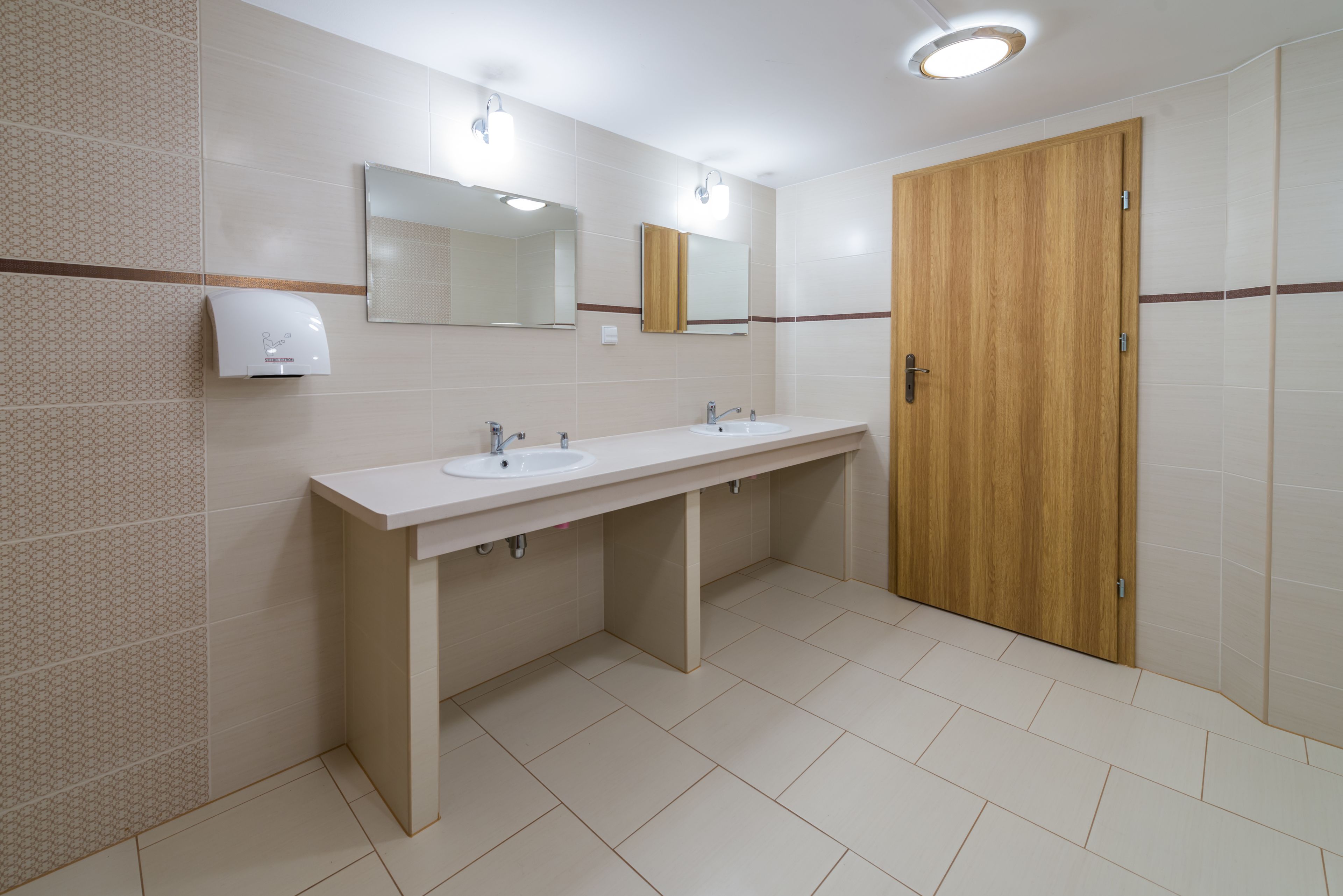 A modern bathroom with two sinks, a mirror, and a wooden door.