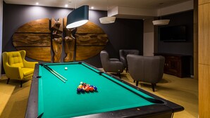 A pool table with balls, a yellow armchair, and two grey armchairs in a room with a large wooden wall art piece and a TV mounted on the wall. - Hotel Wodnik (Gizycko)