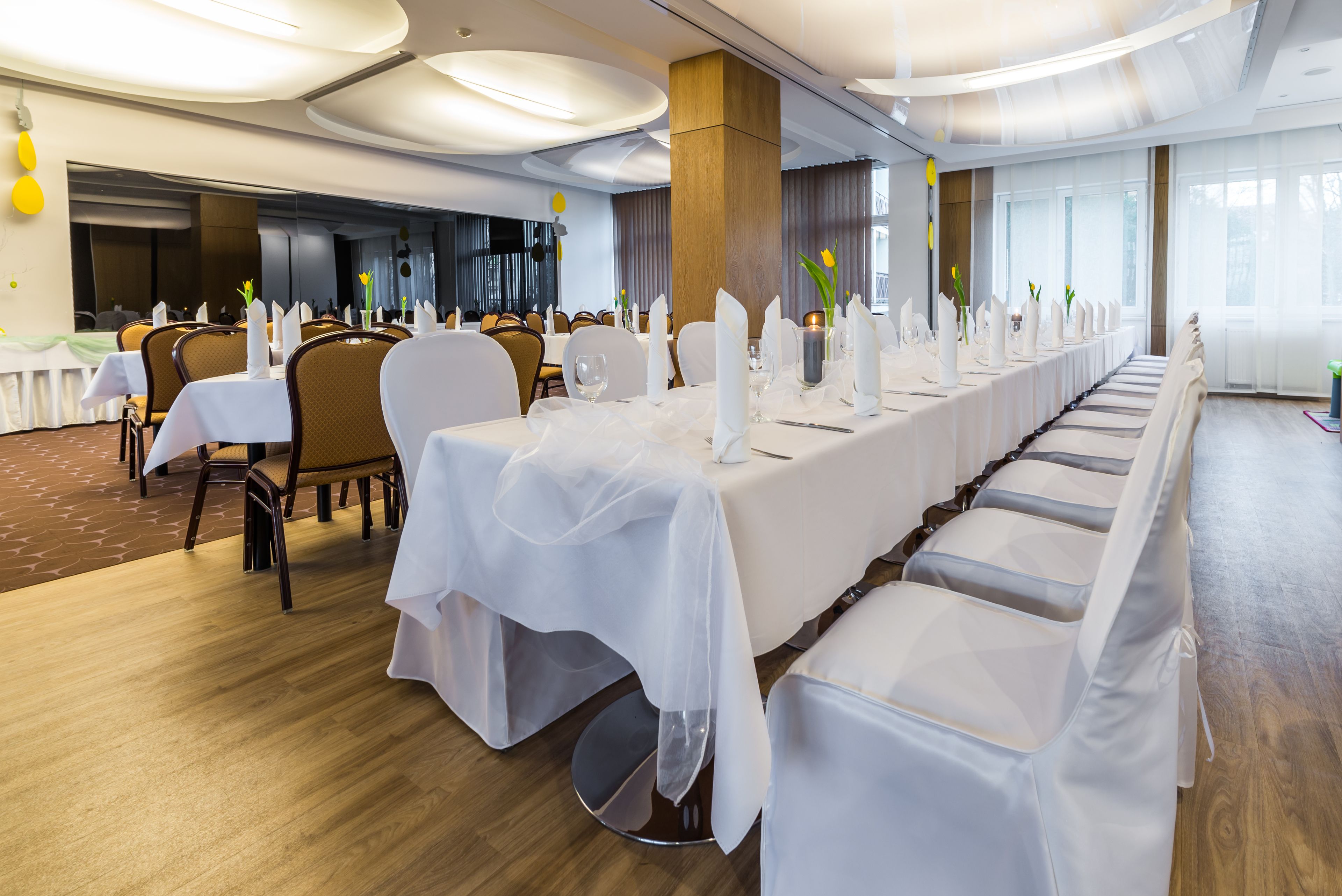 Un salón de banquetes con largas mesas dispuestas para un evento formal, con manteles blancos, sillas y centros de mesa florales.