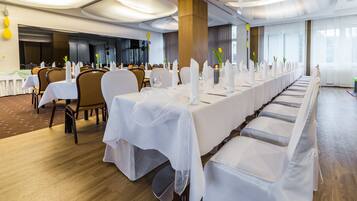 Un salón de banquetes con largas mesas dispuestas para un evento formal, con manteles blancos, sillas y centros de mesa florales.