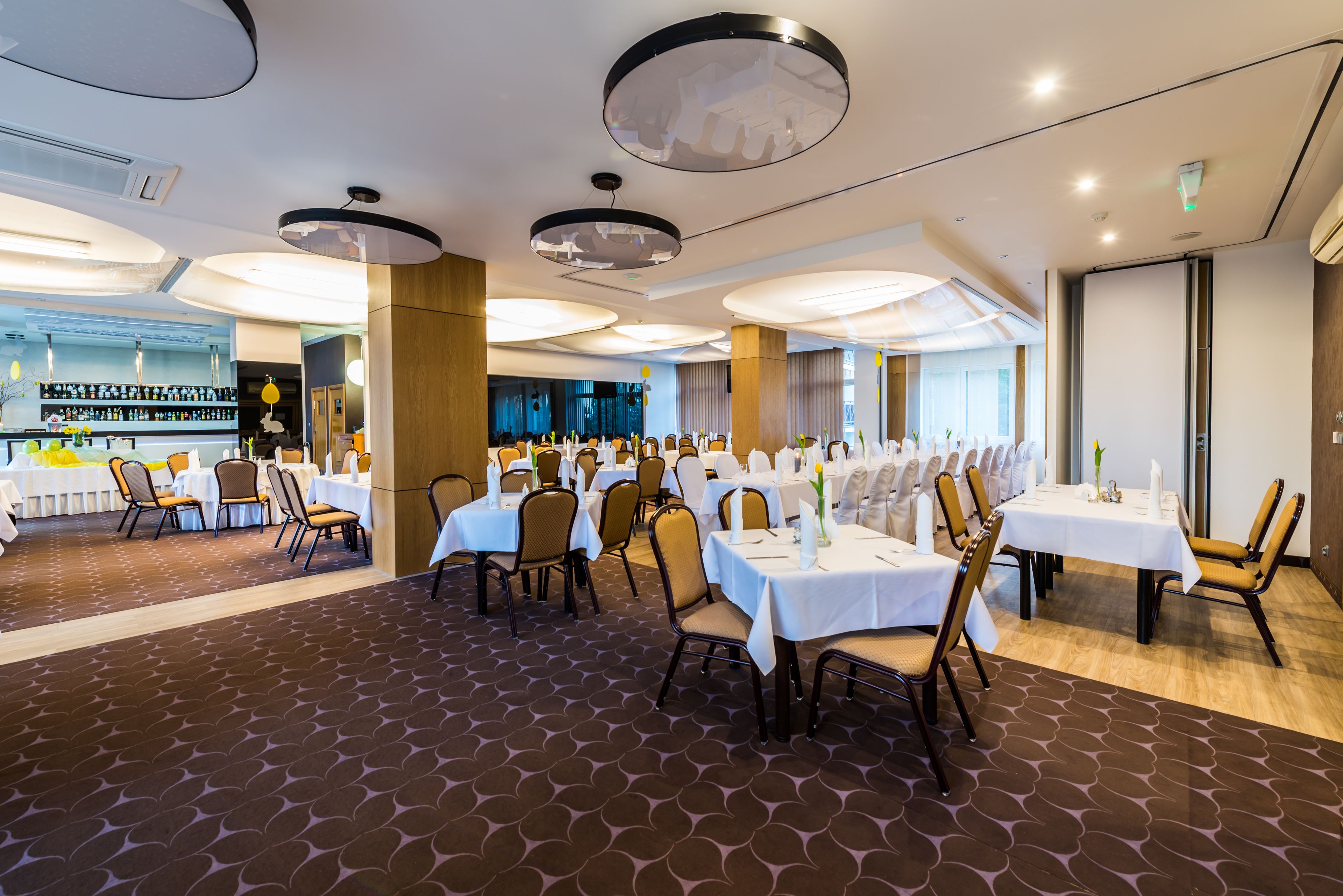 A dining area with round tables, chairs, and a bar in the background.